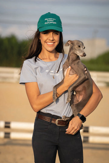 Amazona de hipismo usando boné Mirror Equestrian na cor verde Bottega. Nele esta escrito "Horses are better than people" 